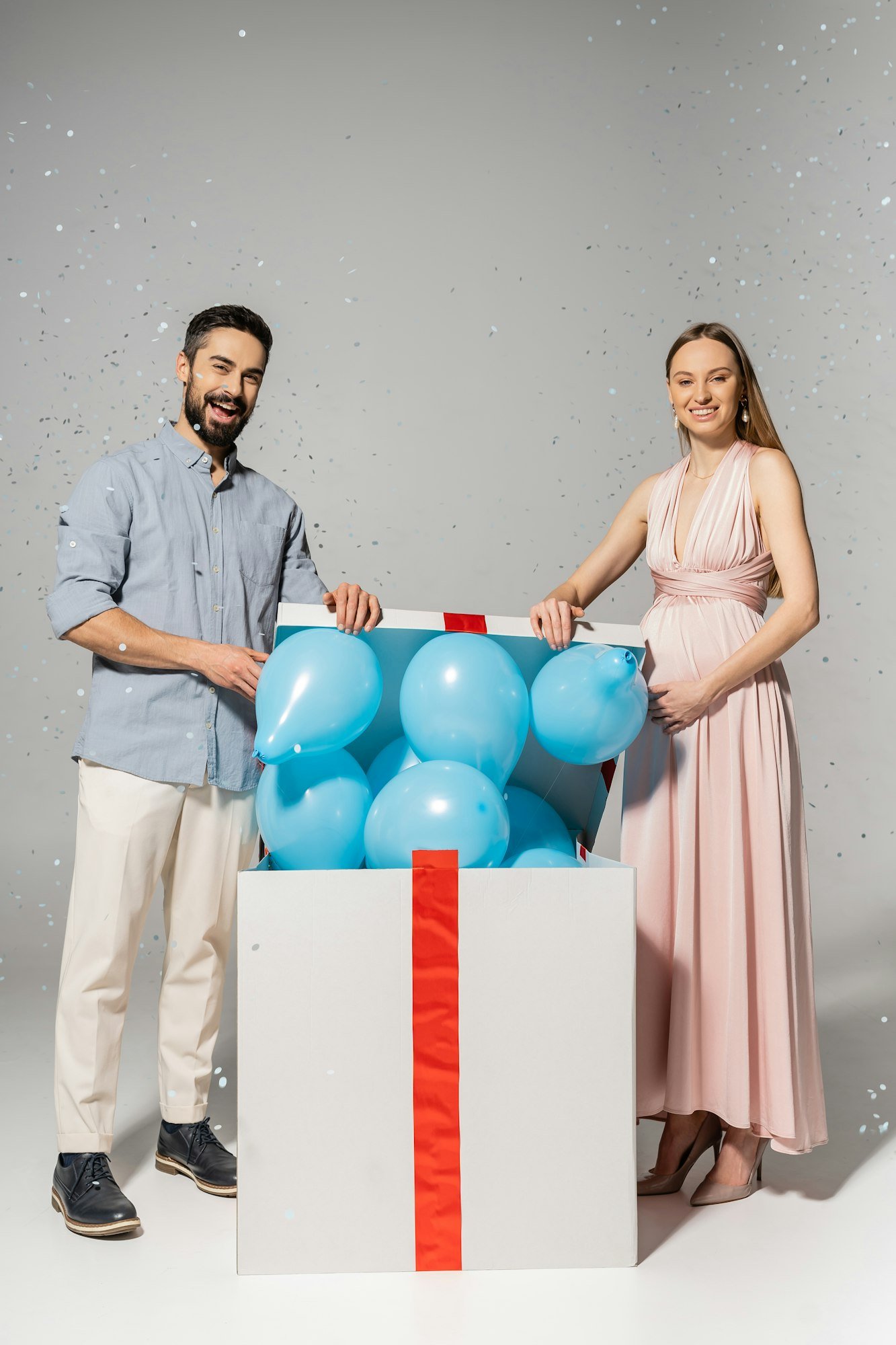 Full length of trendy couple looking at camera while opening gift box with blue balloons | | gender reveal ideas in Dubai, UAE by upshot sfx